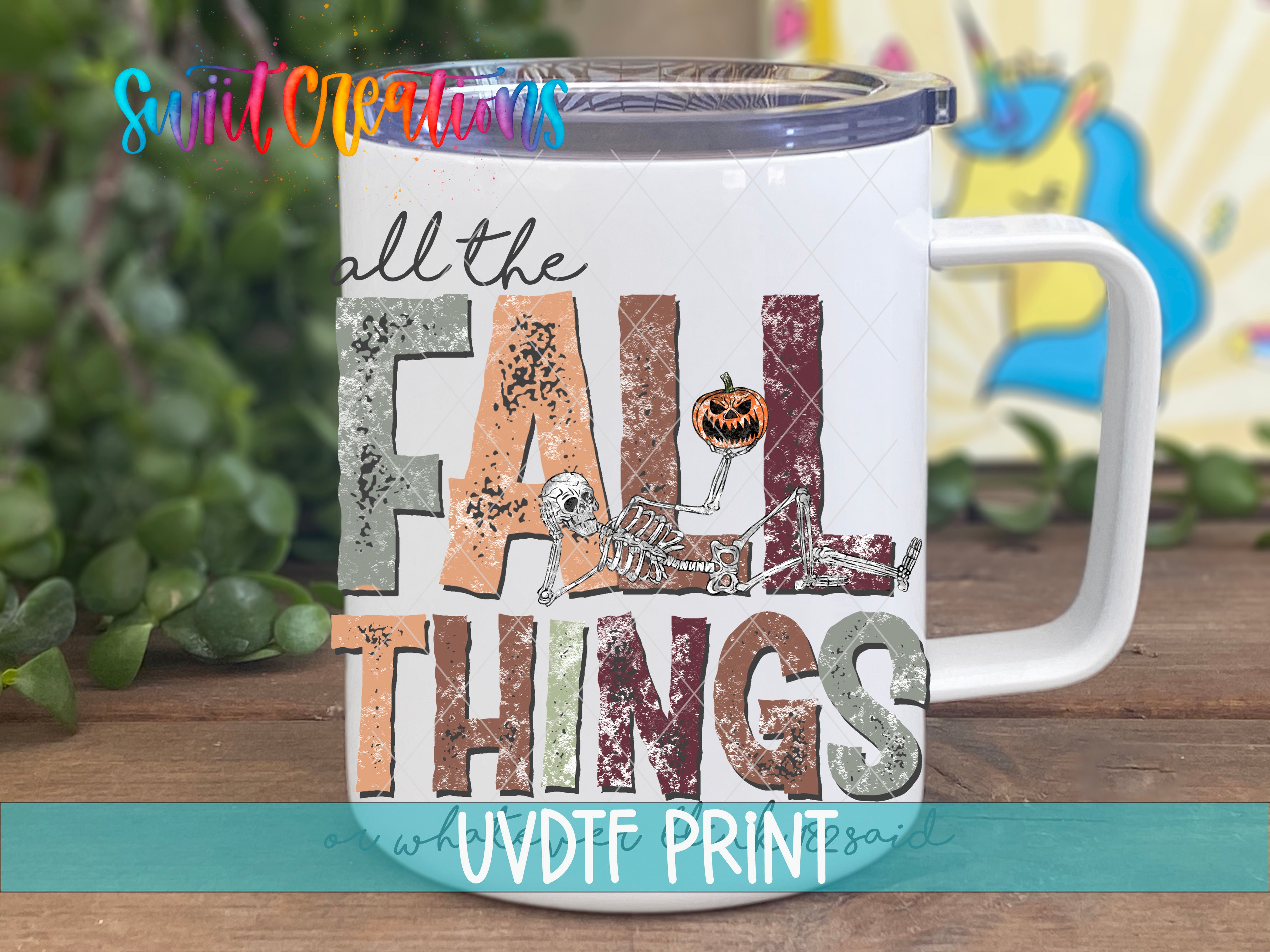 A white mug with a colorful design featuring the text "all the FALL THINGS" and a skeleton figure.