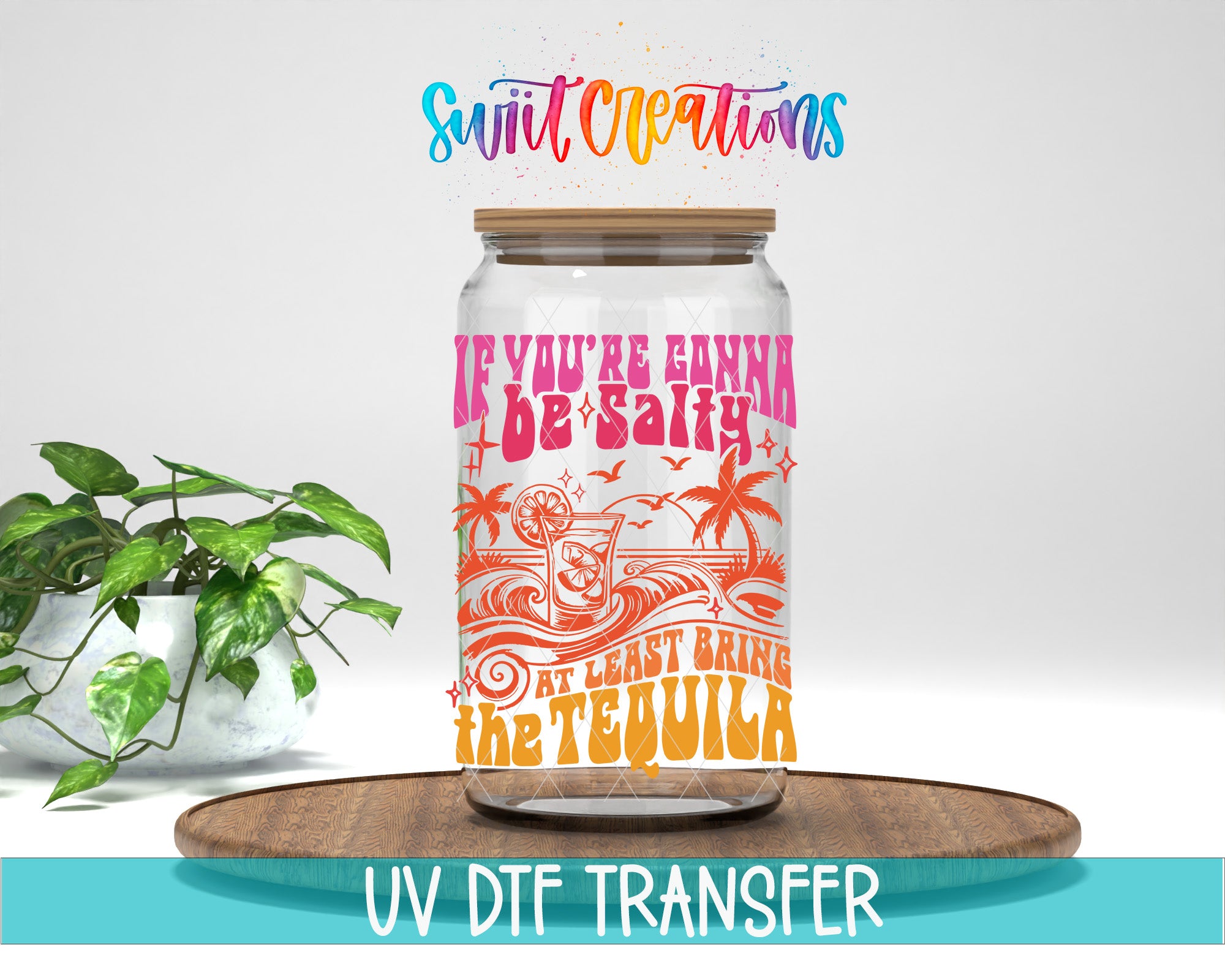 a large glass jar with a colorful design and text, placed on a wooden surface next to a potted plant.