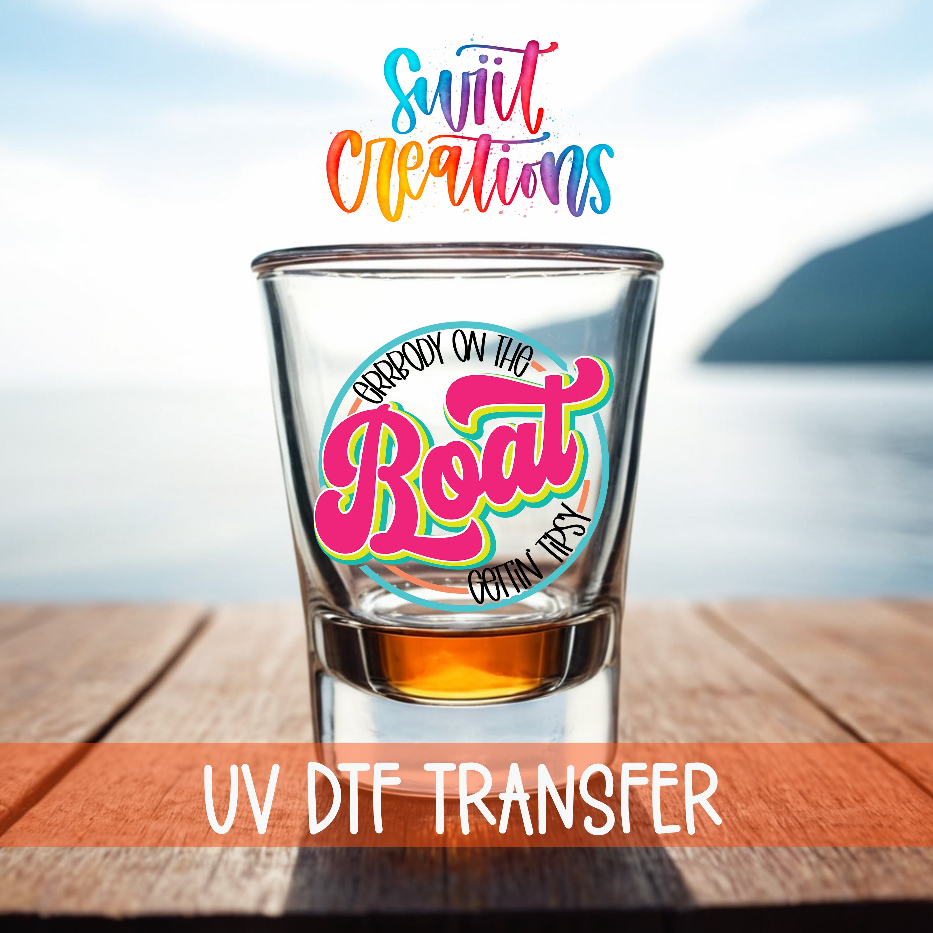 a shot glass with a colorful design on it, placed on a wooden surface with a body of water in the background.
