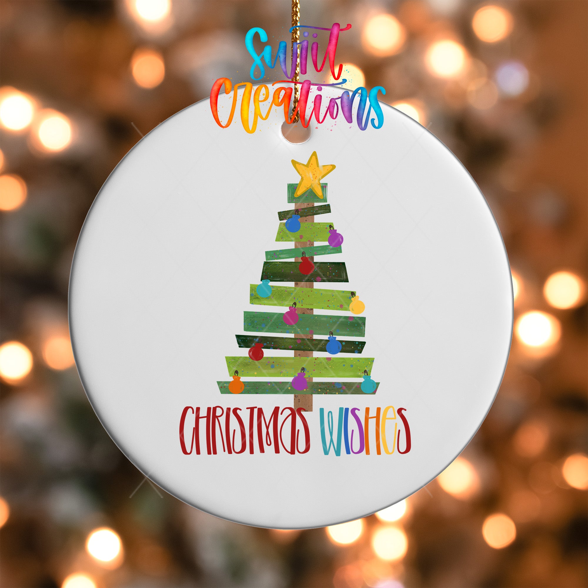 A white Christmas tree ornament with colorful ornaments and a star at the top, hanging against a blurred background with colorful lights.