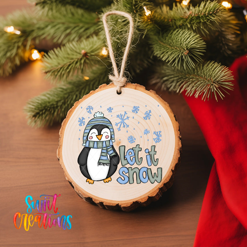 A wooden ornament with a penguin wearing a scarf and hat, surrounded by snowflakes, hangs on a Christmas tree.