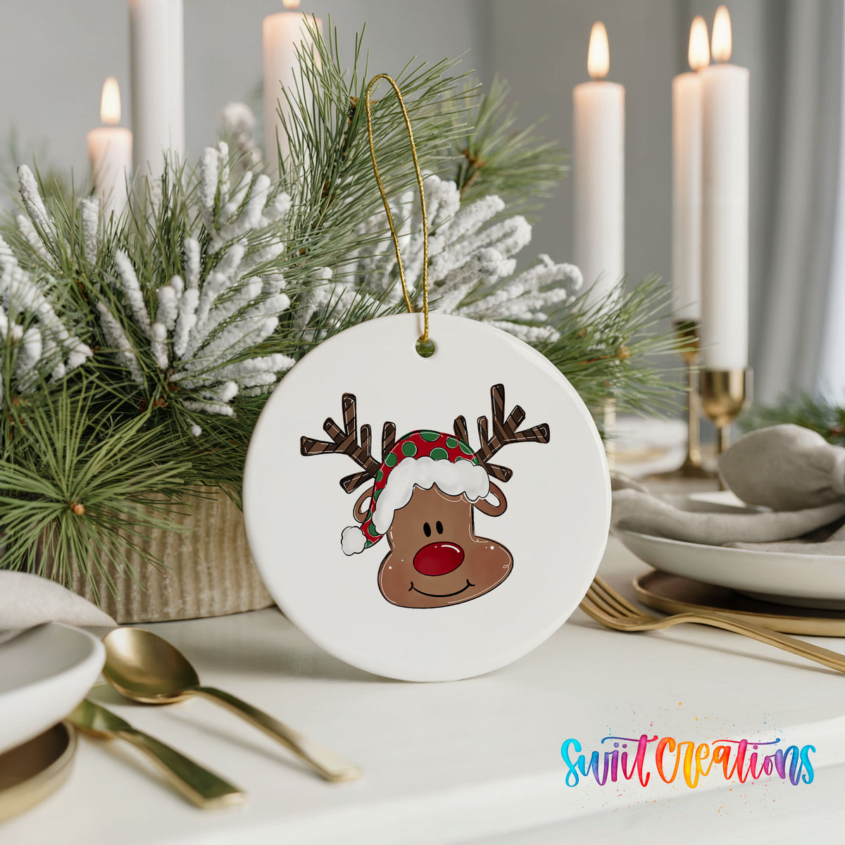 A white ornament with a cartoon reindeer wearing a red and green hat is displayed on a table, surrounded by candles and greenery.