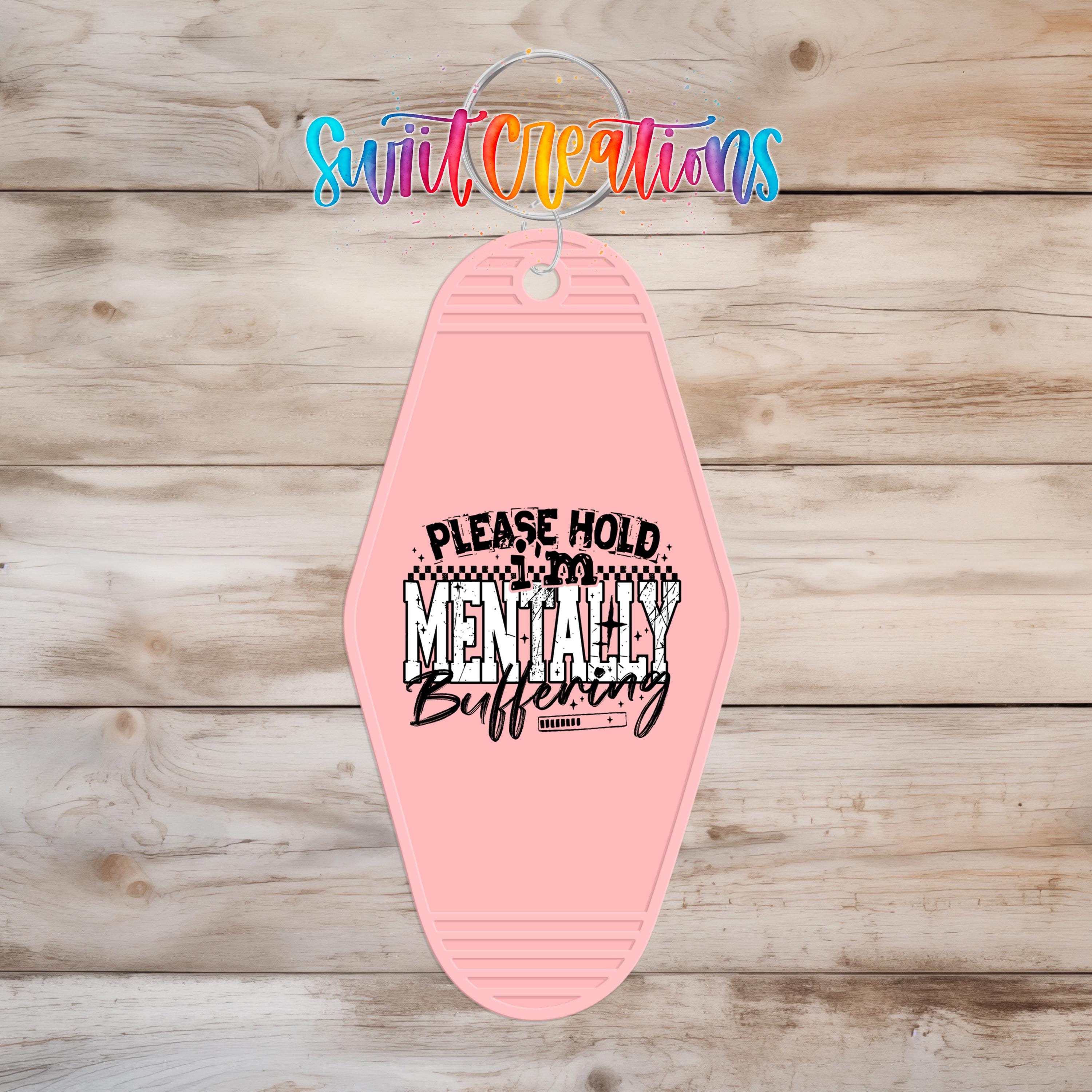 A pink keychain with a humorous text message printed on it, hanging on a wooden surface.