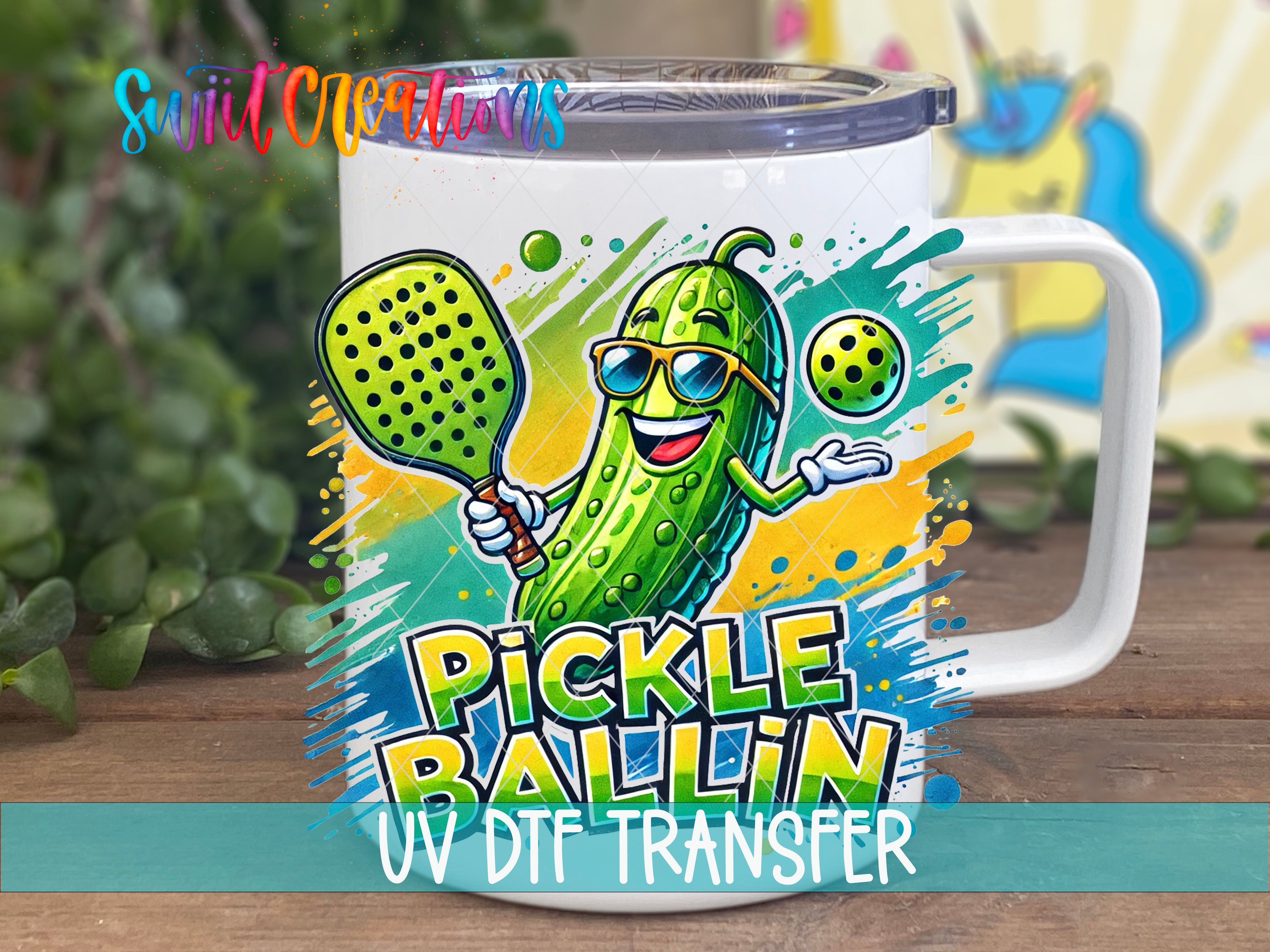 A mug with a cartoon image of a pickle wearing sunglasses and holding a tennis racket, with the text "Pickle Ballin" and "UV DFT Transfer" printed on it.