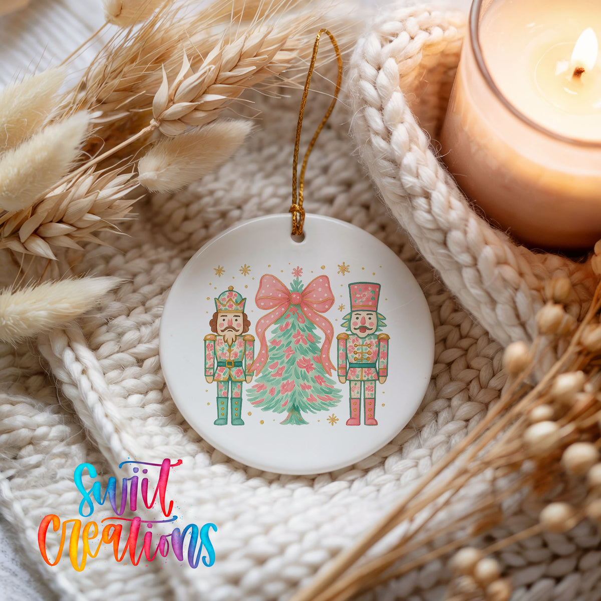 A white ceramic ornament featuring a Christmas tree and two nutcracker characters, hanging on a knitted blanket with a lit candle in the background.