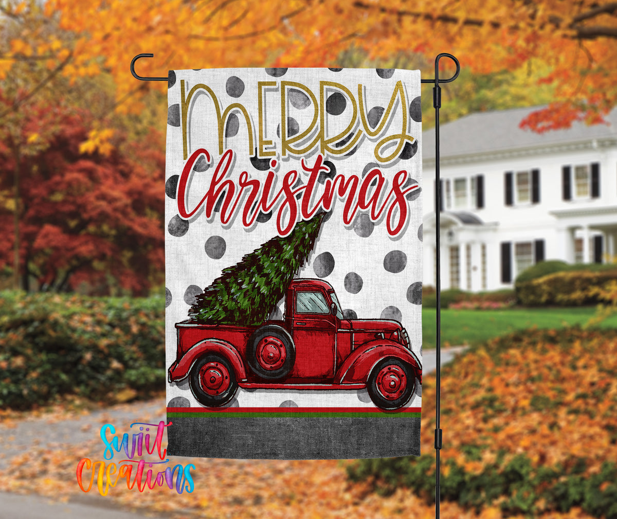 A yard sign with a red truck carrying a Christmas tree, set against a backdrop of autumn foliage.