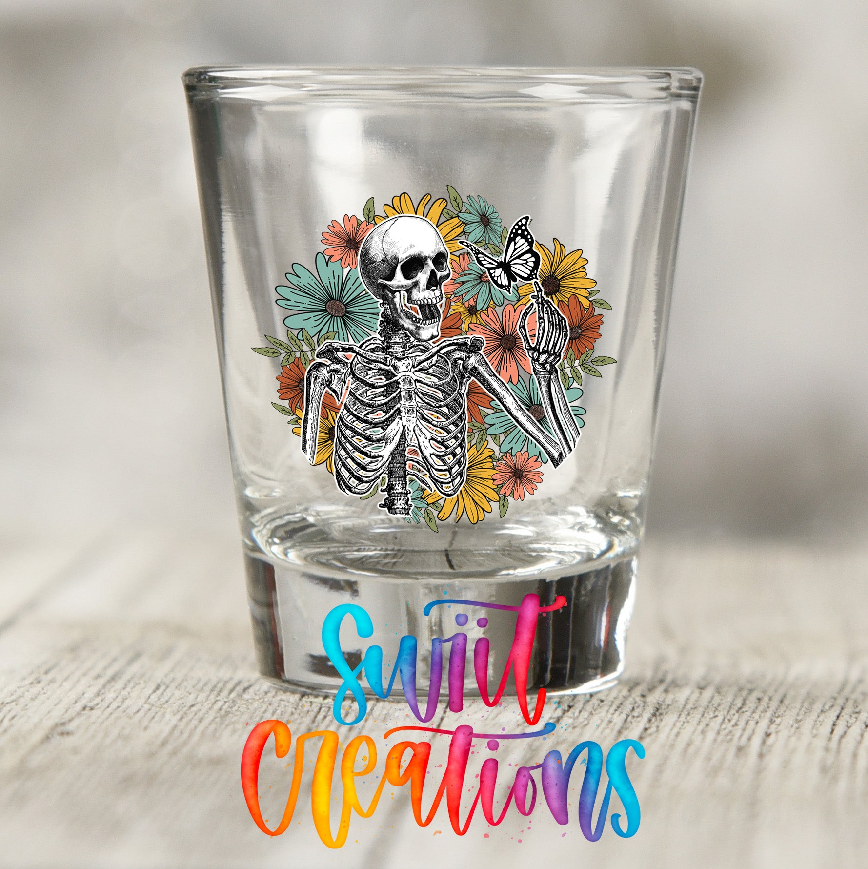 A shot glass with a skeleton and colorful flowers printed on it, along with the text "Sweet Creations" below the image.
