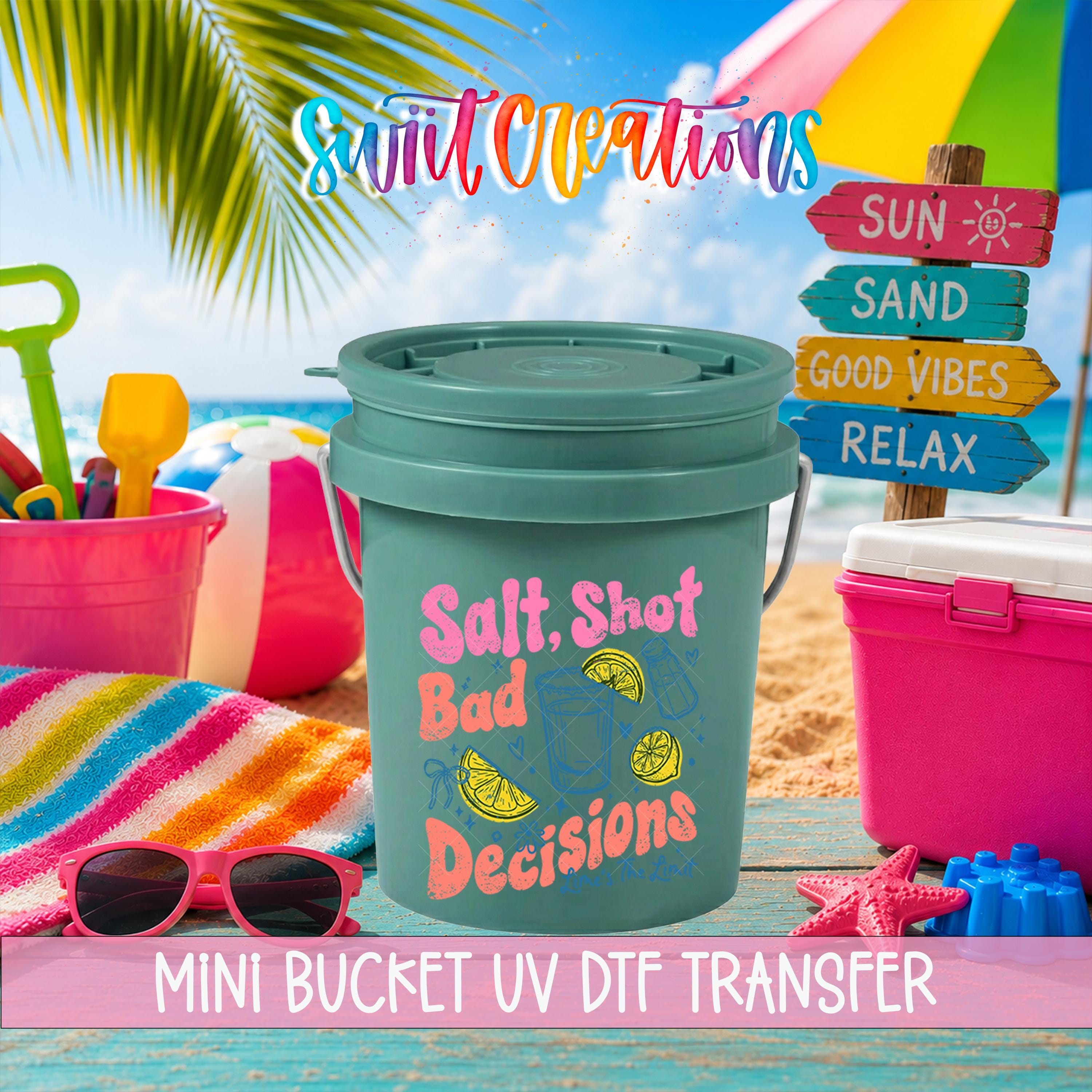 A colorful bucket labeled "Salt. Shot. Bad Decisions" sits on a beach towel, surrounded by beach toys and a sign that says "Sun, Sand, Good Vibes, Relax".