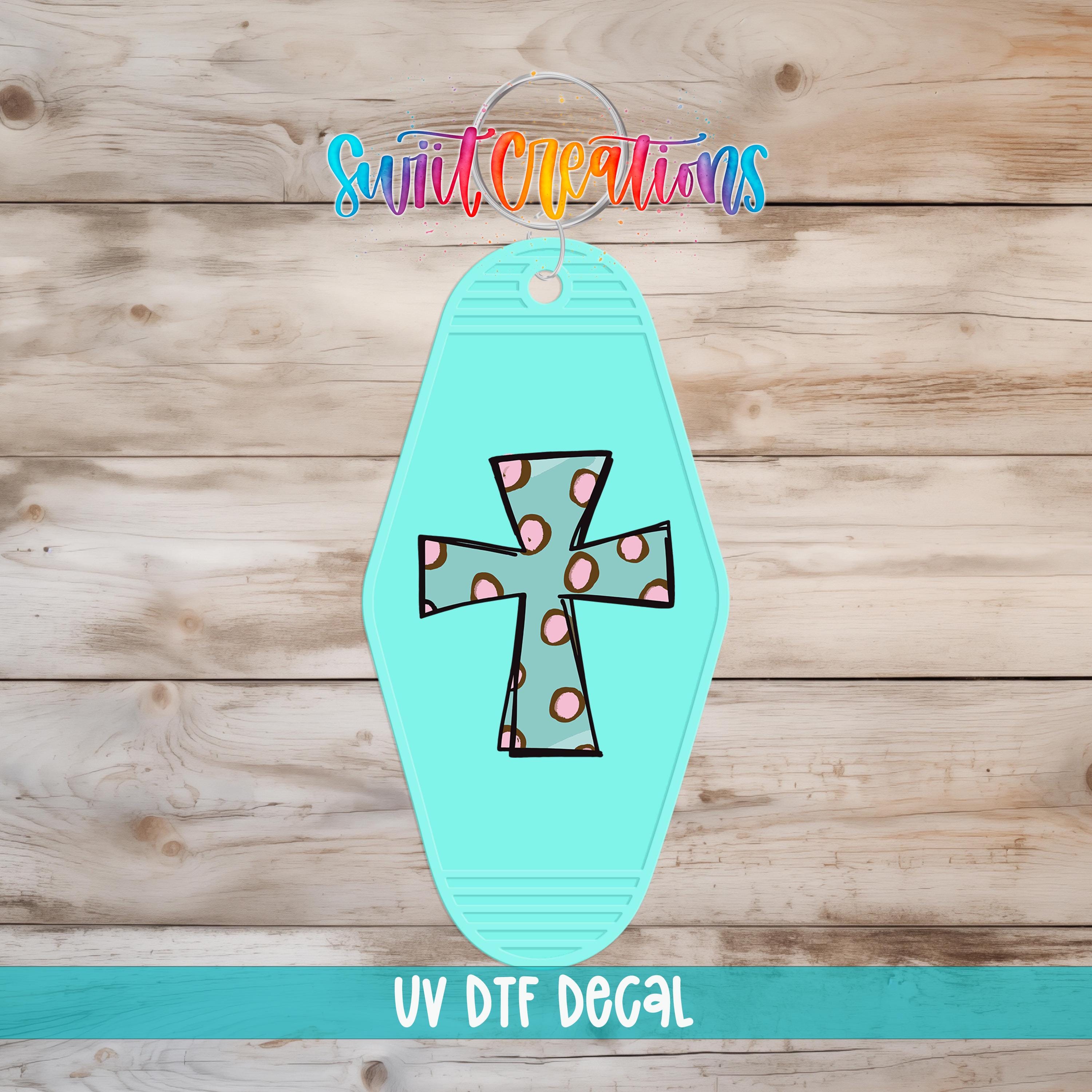 A turquoise cross-shaped keychain with polka dot accents, placed on a wooden surface.