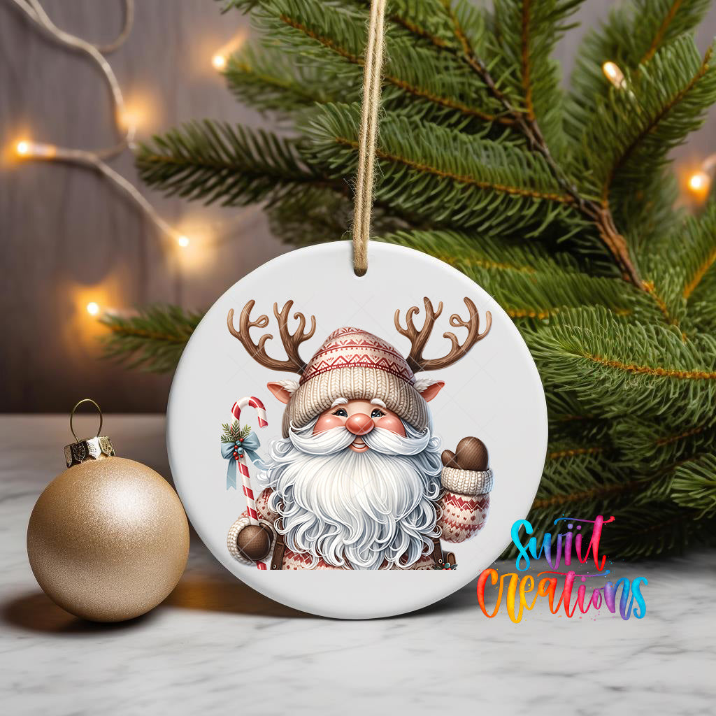 A white ornament featuring a Santa Claus figure with antlers and a red and white striped hat, along with a candy cane and a red and white striped scarf, is displayed on a white surface next to a gold ornament and a Christmas tree.