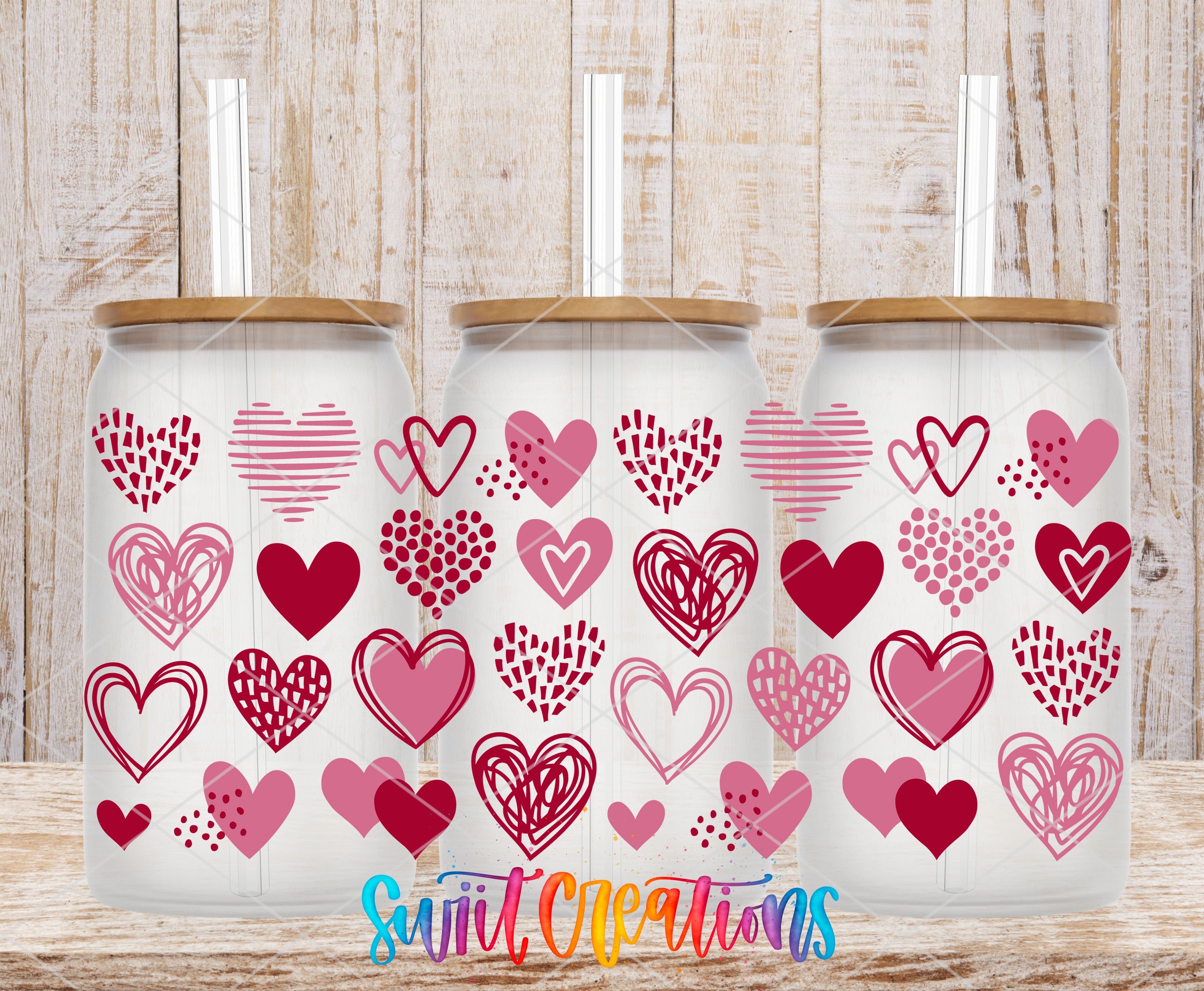 Three glass tumblers with heart-shaped designs on them, placed on a wooden surface.