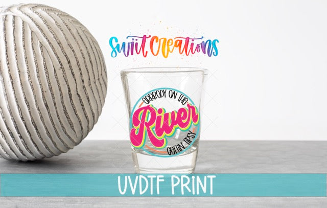 a shot glass with a colorful design and text, placed next to a white ball on a gray surface.
