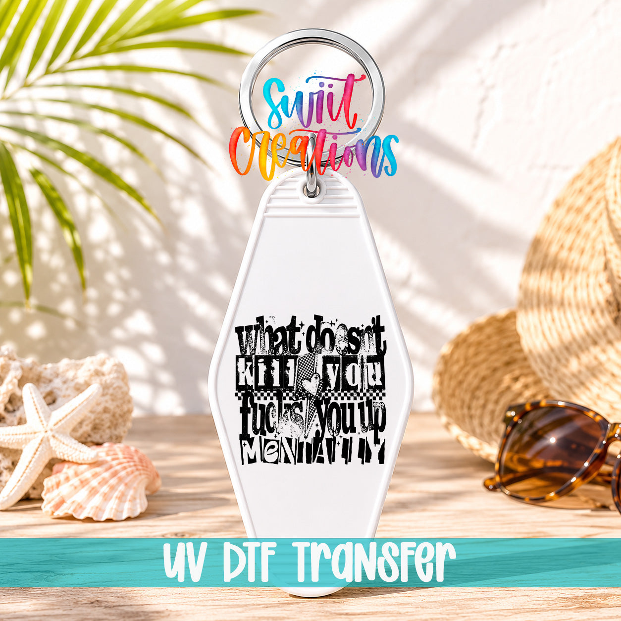 A keychain with a colorful design and text, placed on a wooden surface with sunglasses and a straw hat in the background.