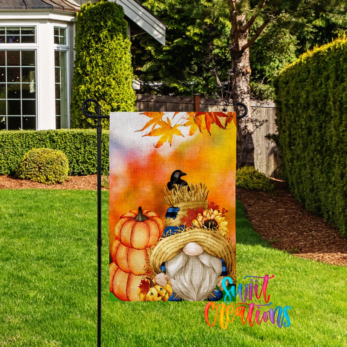 A colorful garden gnome sign with autumn-themed decorations, including pumpkins, a bird, and a straw hat, is displayed in a yard with a house and trees in the background.