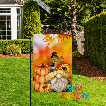 A colorful garden gnome sign with autumn-themed decorations, including pumpkins, a bird, and a straw hat, is displayed in a yard with a house and trees in the background.