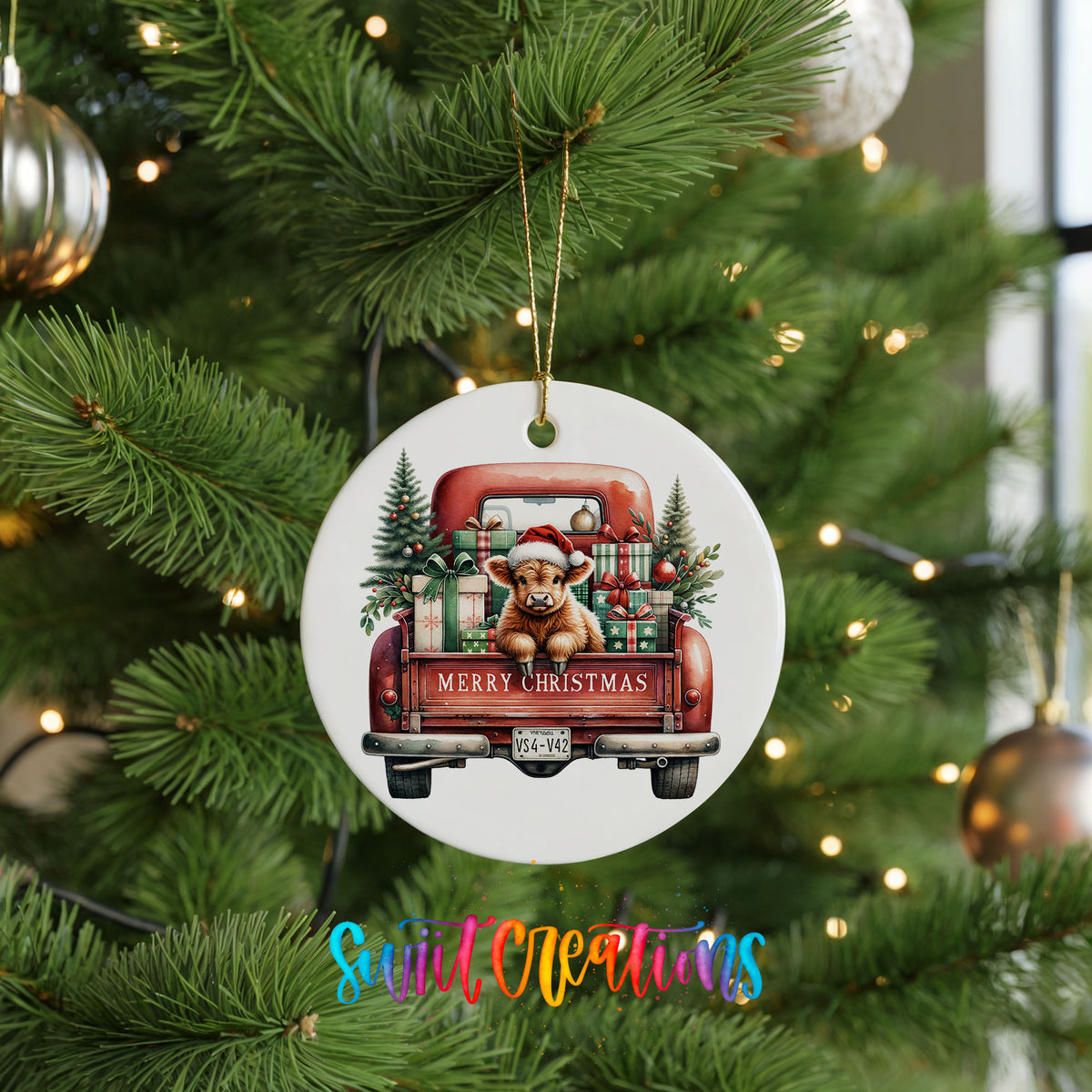 A white Christmas ornament with a red truck and a dog is hanging on a pine tree.