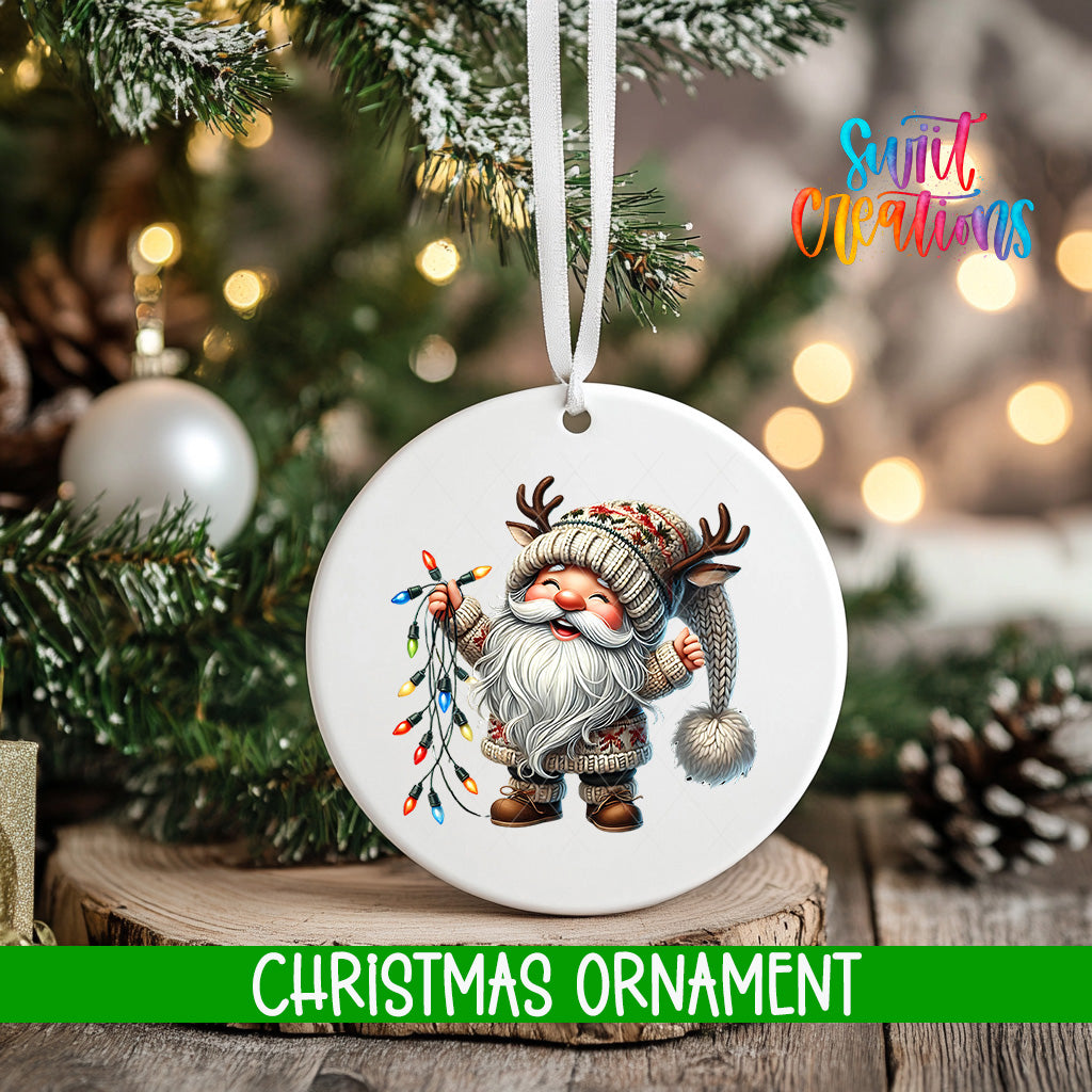 A white Christmas ornament featuring a smiling gnome with antlers, surrounded by colorful lights, is hanging from a tree branch.
