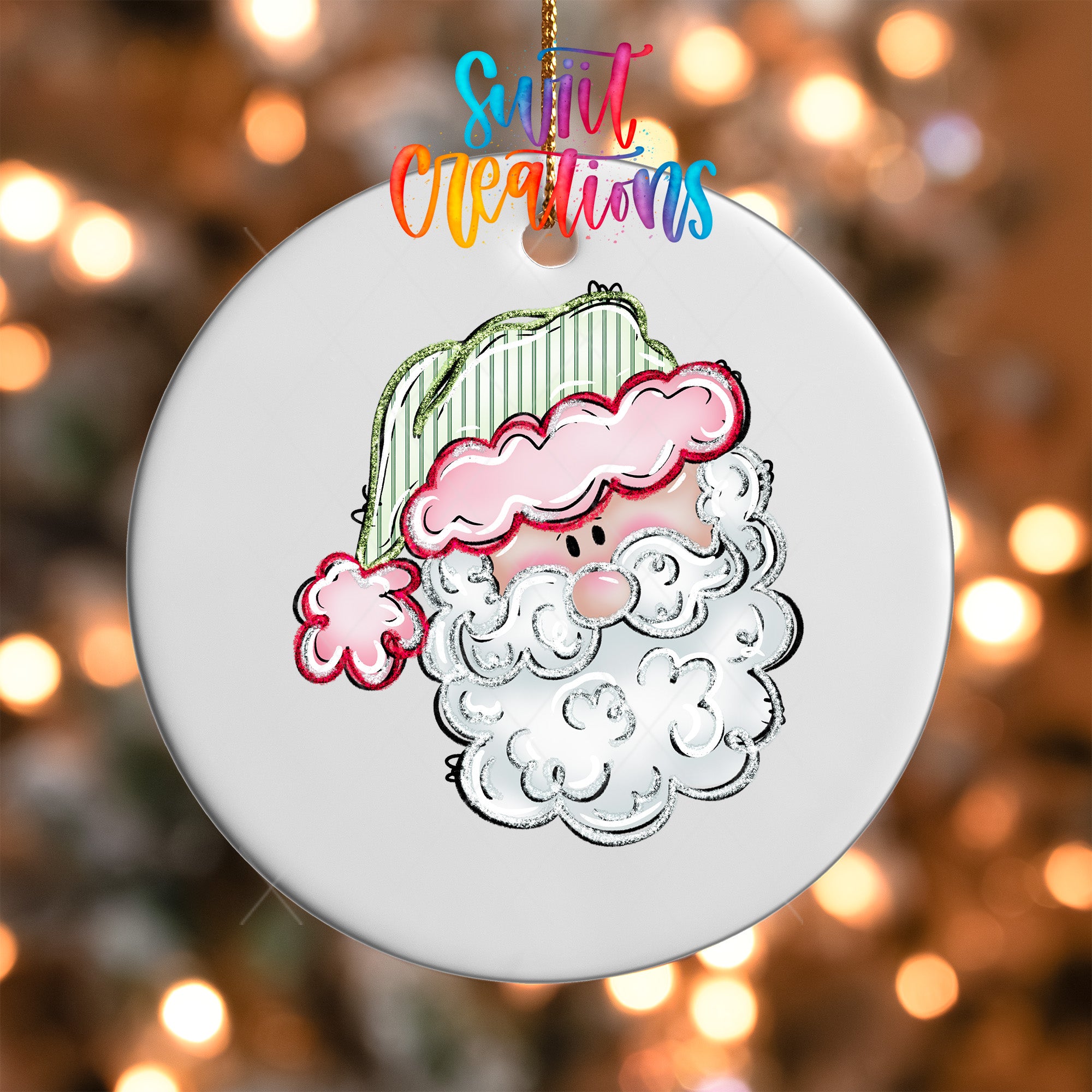 A white ornament with a cartoon illustration of a smiling, white-bearded Santa Claus wearing a green hat with a pink trim.