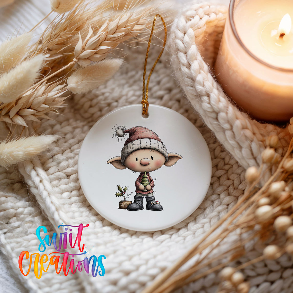A white ornament featuring a cartoon elf wearing a Santa hat and holding a Christmas tree, placed on a white knitted surface next to a lit candle.