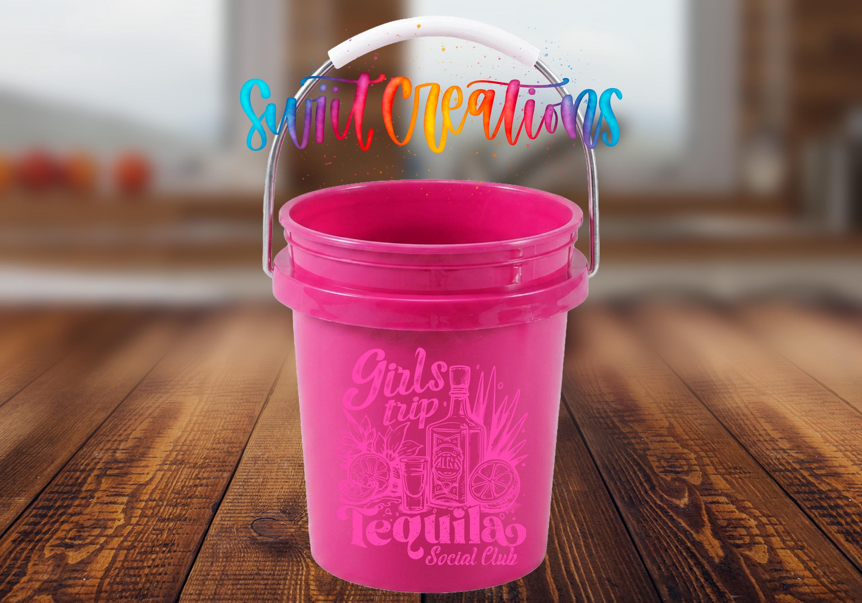 A pink bucket with a handle, featuring a colorful text design and illustrations, placed on a wooden surface.