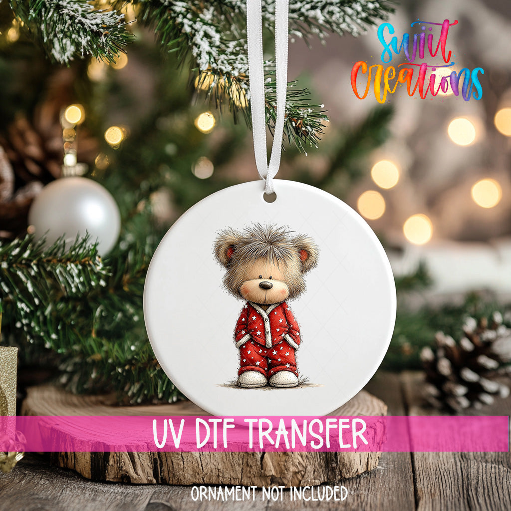 A white ornament with a teddy bear wearing red pajamas is hanging on a Christmas tree.