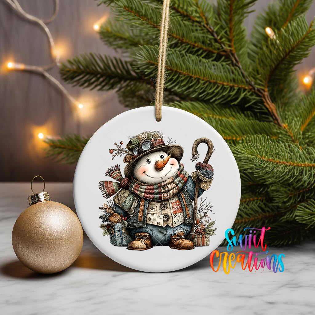 A white ceramic ornament featuring a smiling snowman is displayed on a table, with a gold ornament and a Christmas tree in the background.