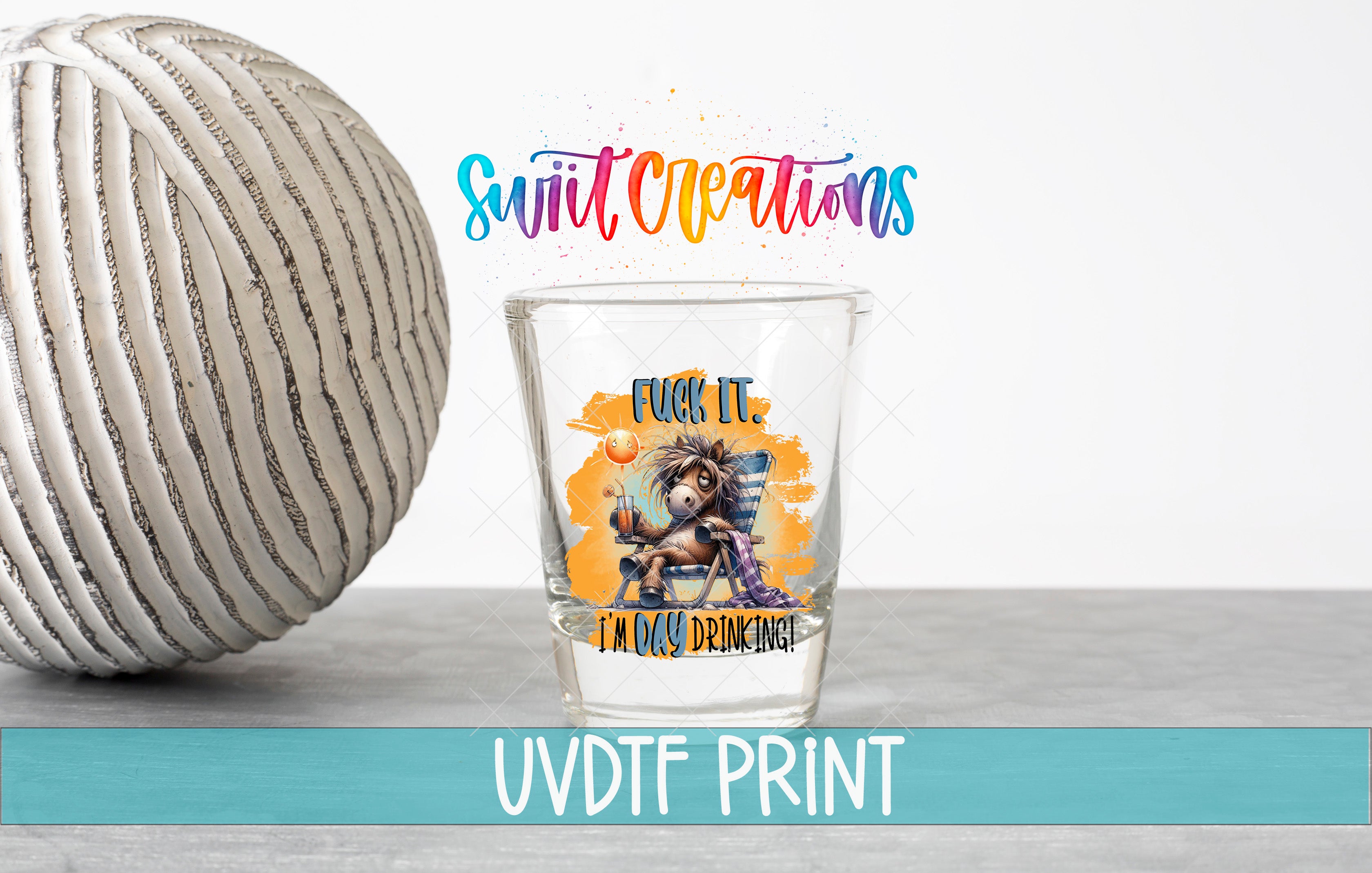 a shot glass with a colorful design and text, placed next to a white ball on a gray surface.