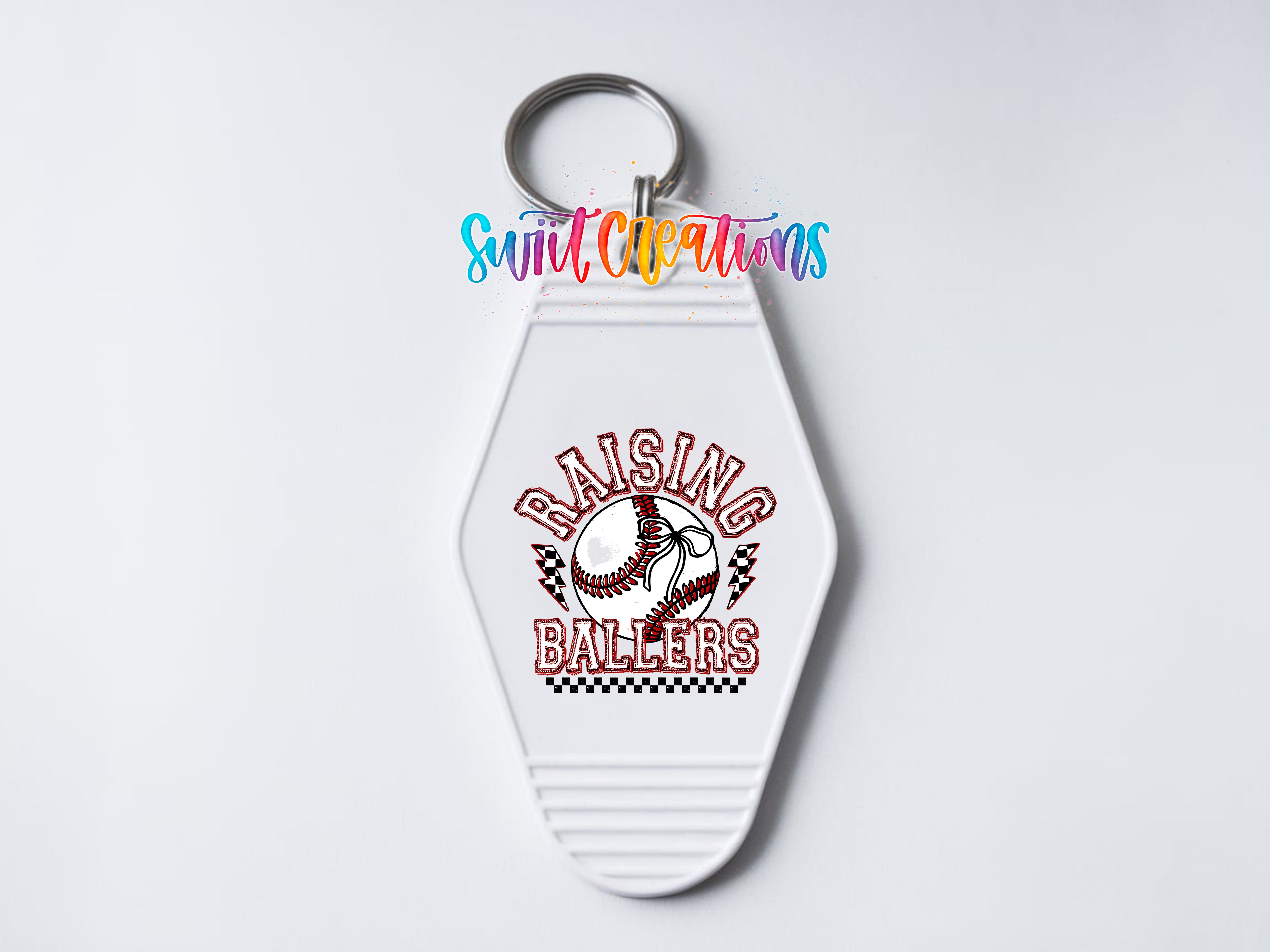 A white keychain with a baseball design and the text "RAISING BALLERS" printed on it.