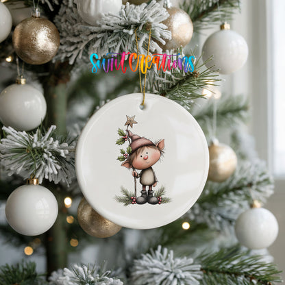 A white ceramic ornament with a cartoon elf on a branch is hanging on a Christmas tree, surrounded by white and gold ornaments.