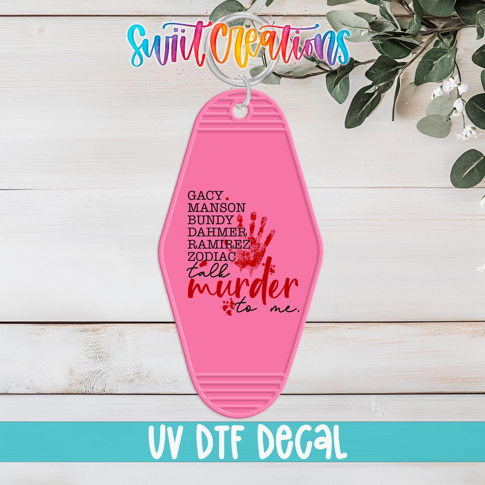 A pink keychain with the text "GACY, MERSON, BUNDY, DADDY, RAMIREZ, ZODIAC, TALM, MURDER, TO ME." printed on it, along with a handprint design. The keychain is displayed on a wooden surface, and there is a plant in the background.