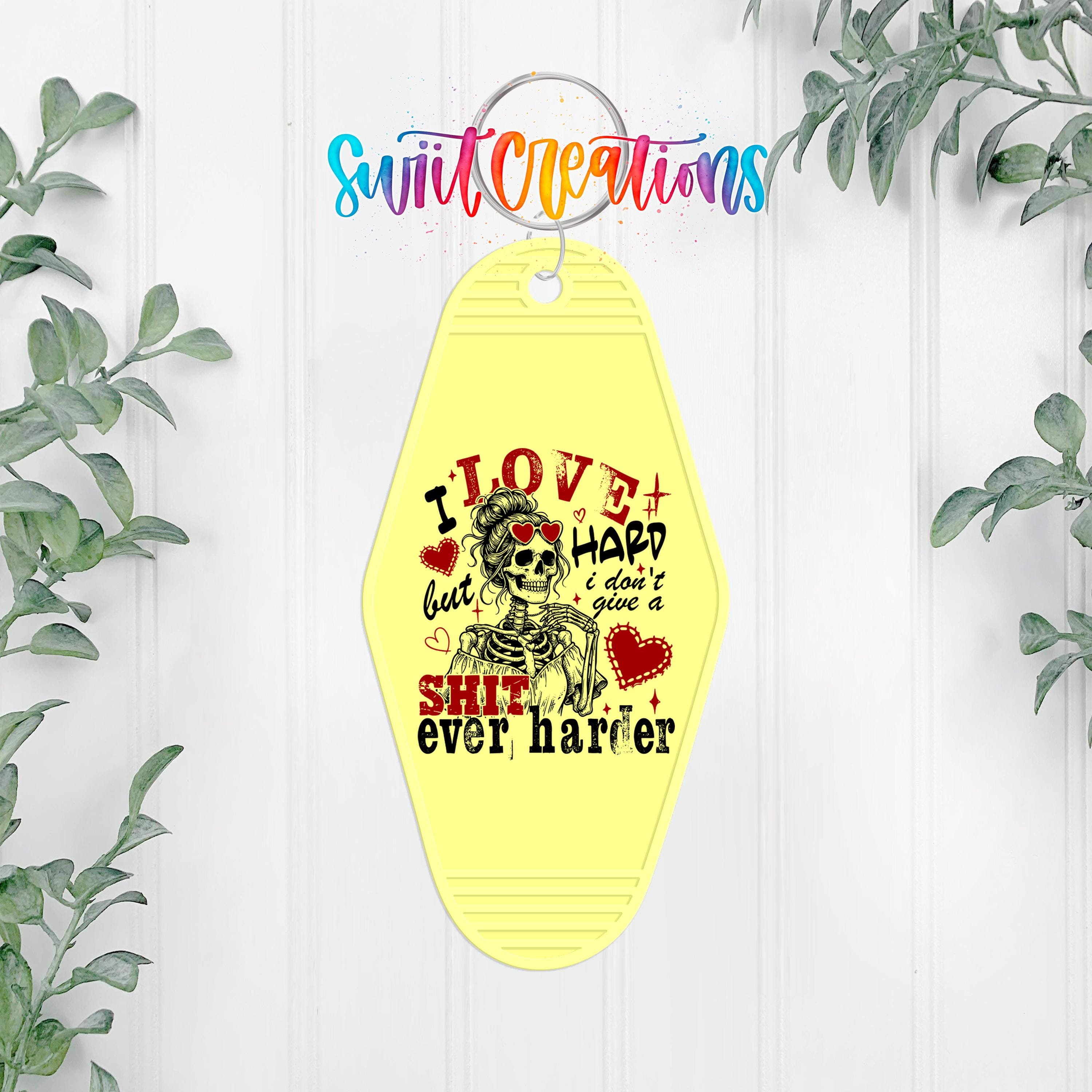 A yellow keychain with a skull design and text that says "I LOVE but I HARD I DON'T give a SHIT ever harder".