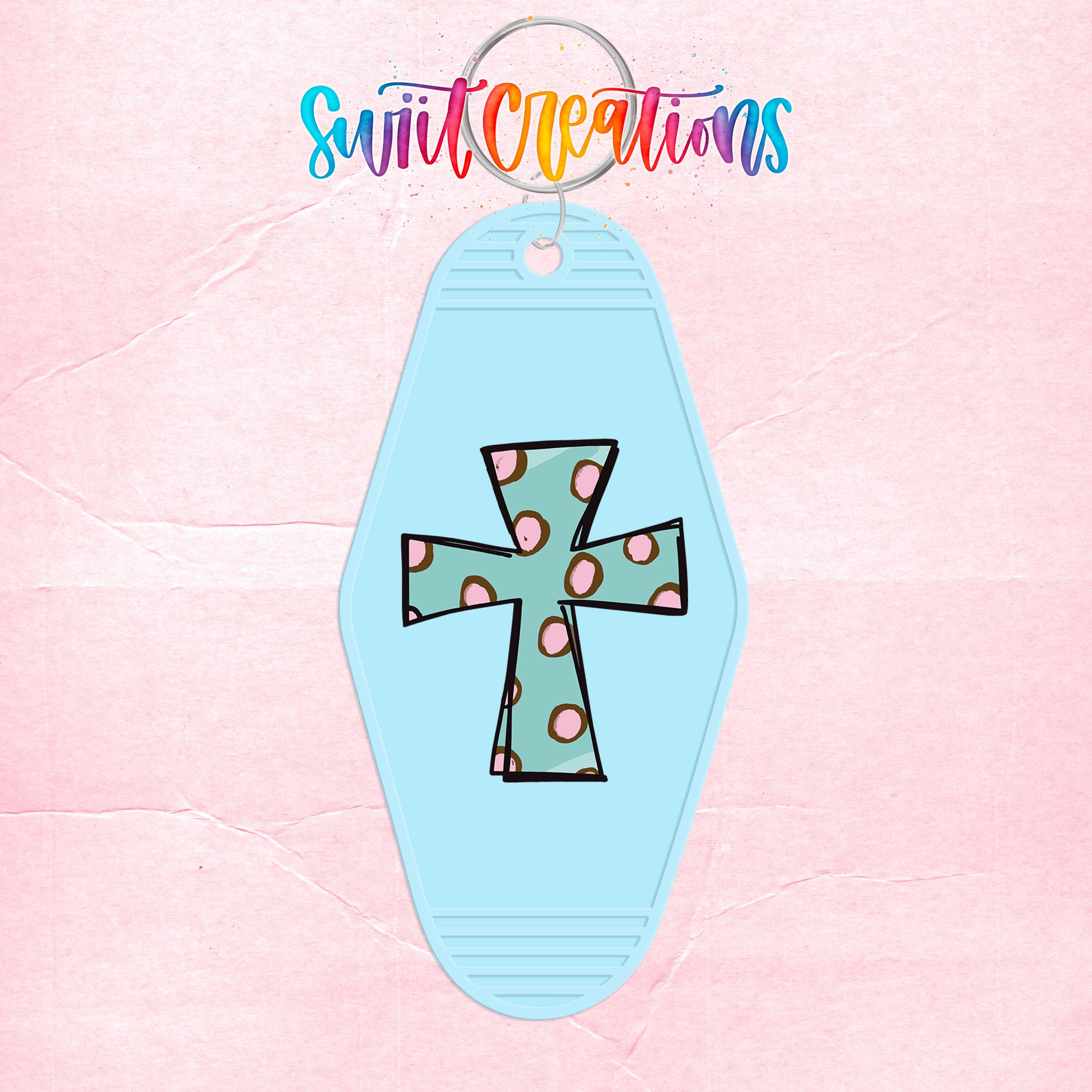 A keychain with a cross design and colorful polka dots is shown against a pink background.