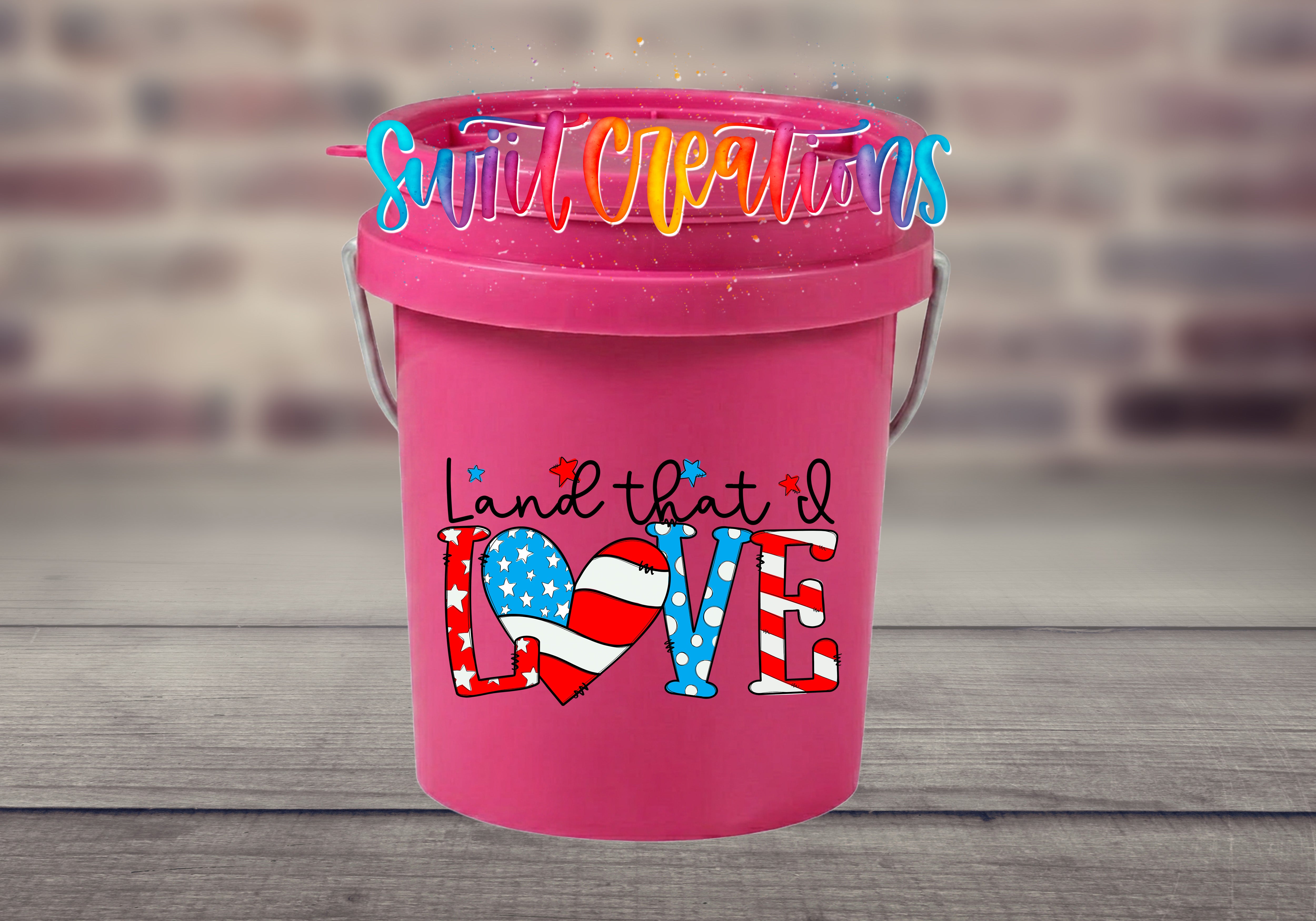 A pink bucket with a colorful design and text on it, placed on a wooden surface.