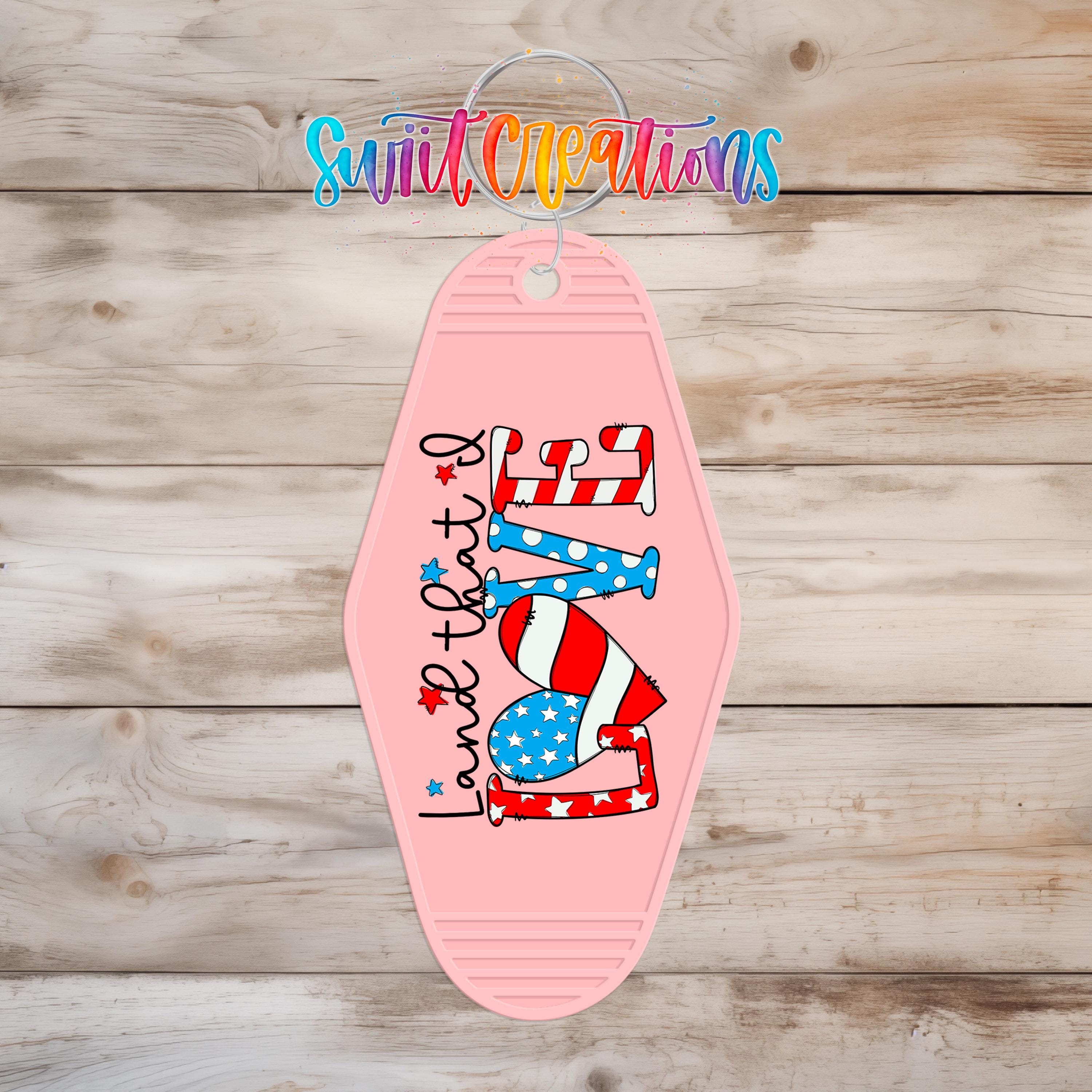 A pink keychain with the text "Land that I love" printed on it, featuring an American flag design.