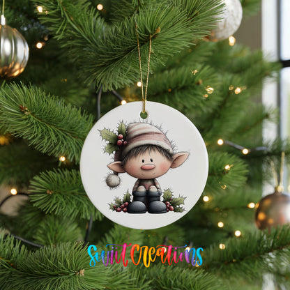 A white ornament featuring a cartoon elf sitting on a branch, surrounded by greenery and berries, is hanging from a Christmas tree.
