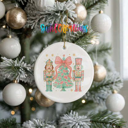 A white ceramic ornament with a Christmas tree design and two nutcracker characters is hanging on a decorated Christmas tree.