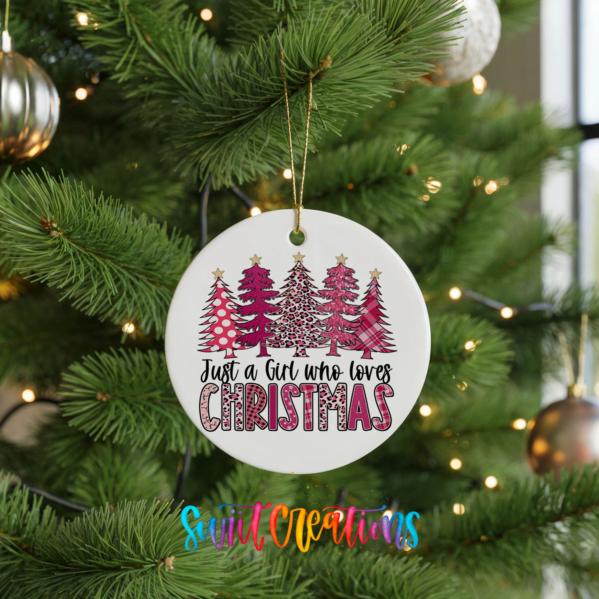 A Christmas tree decorated with ornaments, including a white ornament with a design of pink and white trees and the text "Just a Girl Who Loves Christmas".