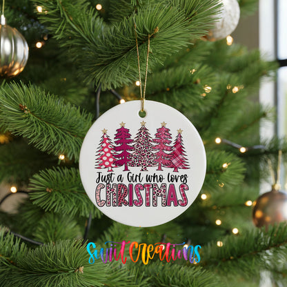 A Christmas tree decorated with ornaments, including a white ornament with a design of pink and white trees and the text "Just a Girl Who Loves Christmas".