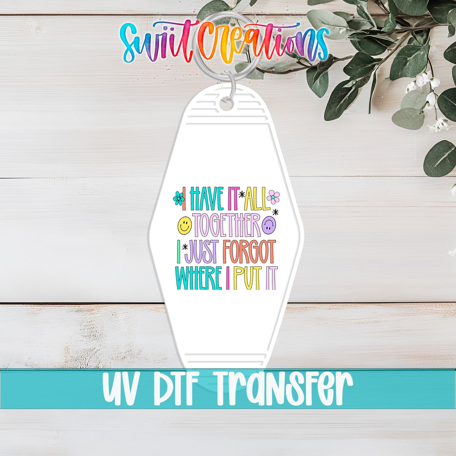 A keychain with a colorful design and text, placed on a wooden surface with some greenery in the background.