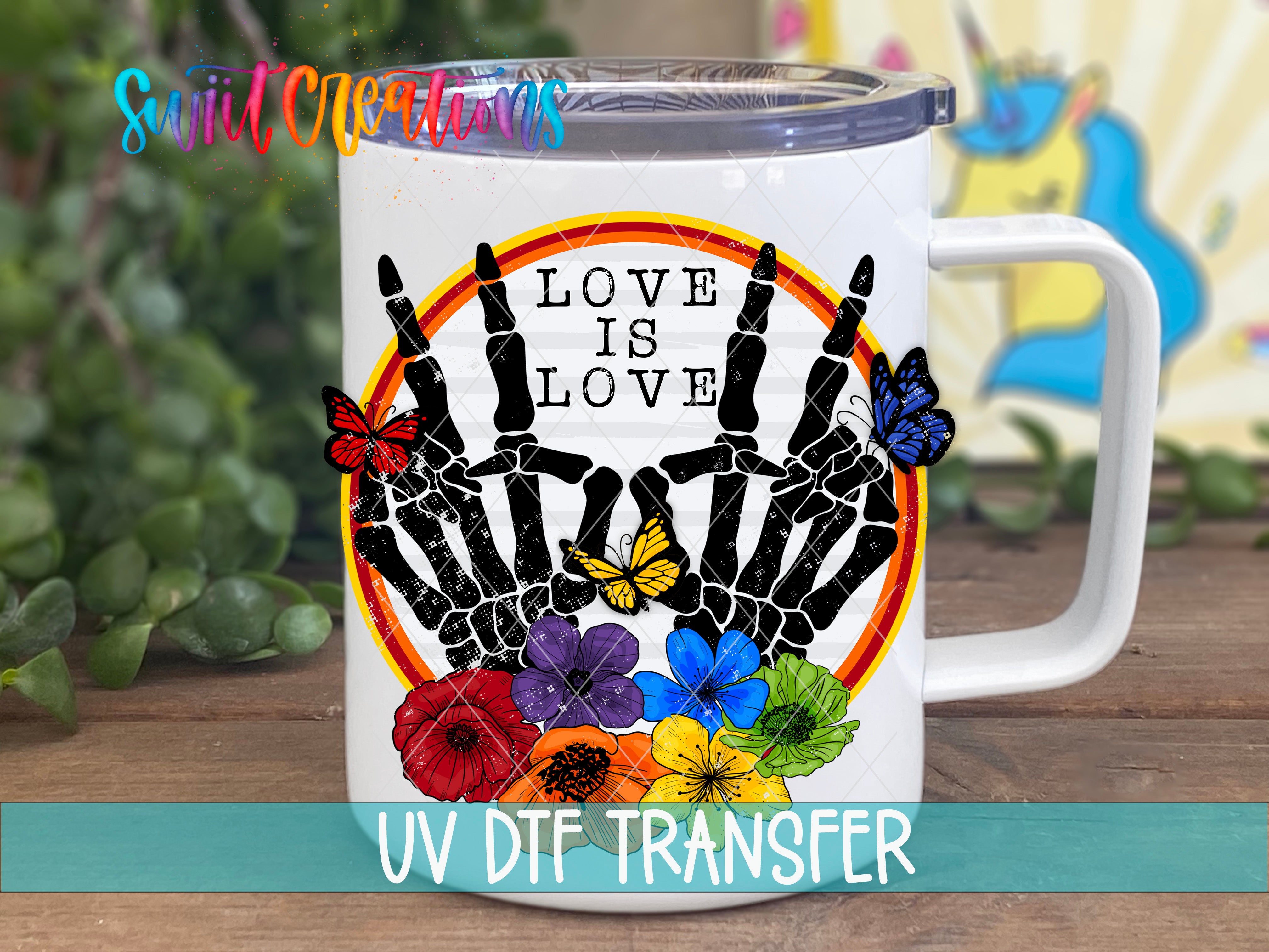 A white mug with a colorful graphic design featuring a skeleton hand holding up a flower and butterflies, surrounded by a circular border with the text "LOVE IS LOVE" and a rainbow-colored background.