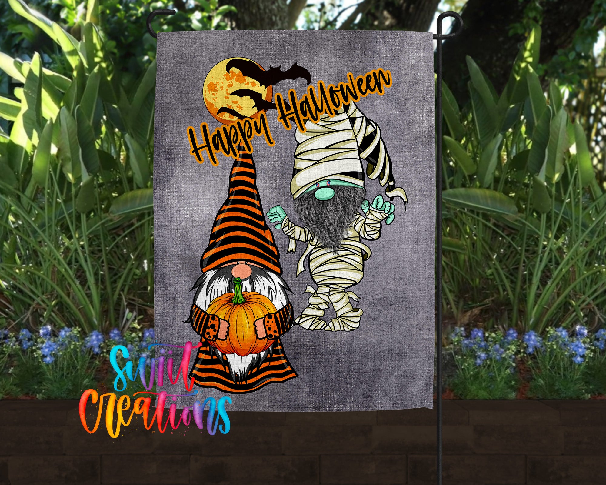 A Halloween-themed garden flag featuring two gnomes, one dressed as a mummy and the other as a gnome, holding pumpkins and surrounded by plants.