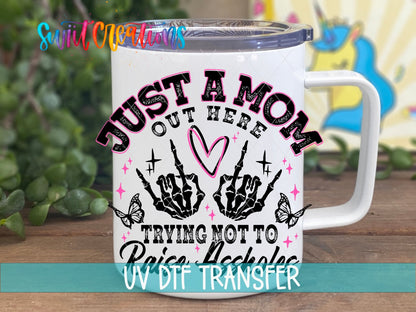 Just a Mom Trying Not To Raise Assholes UV DTF transfer displayed on a white coffee mug from Swiit Creations